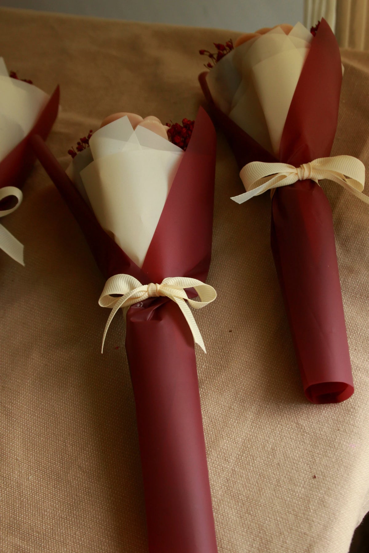  Miniaturowy bukiecik ze świecami sojowymi w kształcie róż, zapakowany w papier bordo i kremowy z kremową wstążką – eleganckie podziękowanie dla nauczyciela
